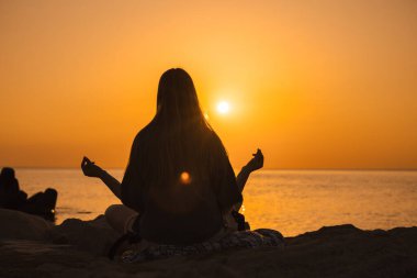 Gün doğumunda deniz kıyısında meditasyon yapan genç bir kadın, Mudra 'da elleri nilüfer pozisyonunda oturuyor, iç huzuru, enerjiyi ve doğayla uyum içinde buluyor. Yüksek kalite fotoğraf