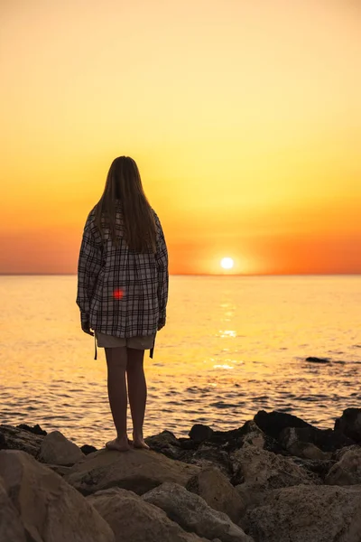 Gün batımında kıyıdaki kayalıklarda durup ufka bakan bir genç. Yüksek kalite fotoğraf