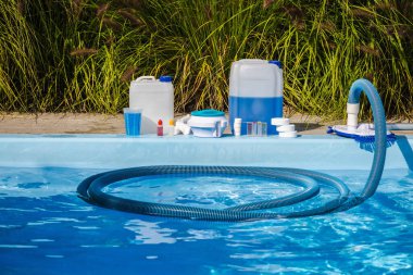 Suyun içinde vakumlu hortumla yüzme havuzu temizleme, kimyasal kutular, klor tabletleri, şeker kutusu, havuz kenarına yerleştirilmiş ölçüm kabı ve test seti gibi bakım ürünleri. Yüksek kalite fotoğraf