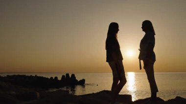 Anne ve genç kız gün batımında deniz kıyısında el ele tutuşuyorlar. Yüksek kalite 4k görüntü