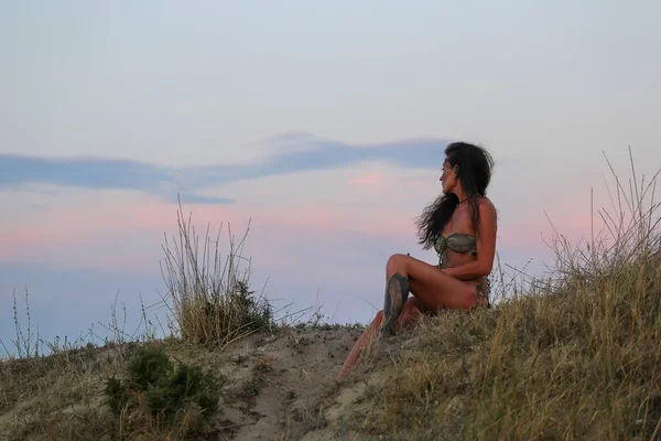 Woman in a bathing suit with tattoos near the sea against the evening sky