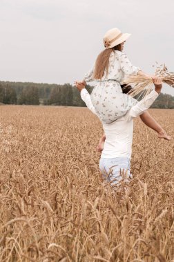 genç neşeli bir çift portresi, şapkalı bir kız buğday kulakları bir buket ile bir adamın omuzlarında oturur