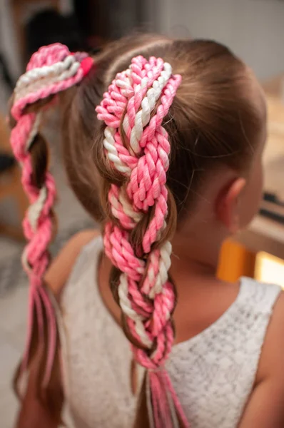 Handmade elastic hair band with colored pigtails made of artificial hair on a little girl with blond hair