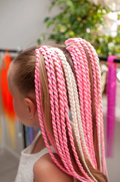 Handmade elastic hair band with colored pigtails made of artificial hair on a little girl with blond hair