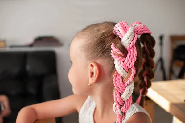 Handmade elastic hair band with colored pigtails made of artificial hair on a little girl with blond hair