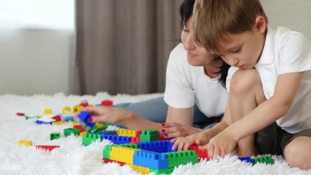 Matka a dítě odpočívají na posteli. Šťastná rodina hraje s mekano barevnými bloky.