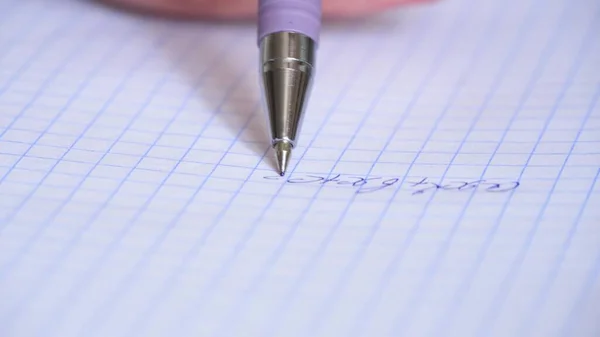 The hand holds a pen and writes a mathematical formula in a notebook. Solution of equation.