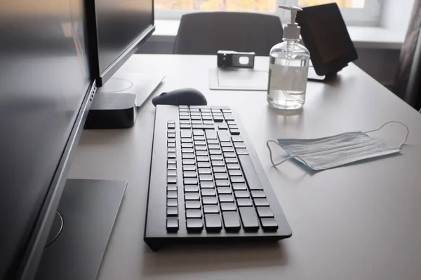 Antiseptic and medical mask on the desktop with a computers, desk, keyboard. Protection from coronavirus COVID-19. Disinfection of the workplace.