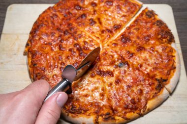 Bir margherita pizzasını pizza bıçağıyla kesiyor.