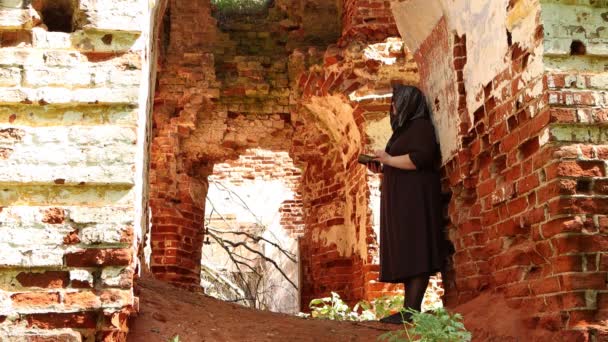 No arco da igreja arruinada está uma mulher idosa com uma bíblia nas mãos . — Vídeo de Stock