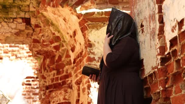 Uma mulher idosa em uma igreja encostada a uma parede, ela lê uma oração . — Vídeo de Stock