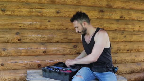 Closeup man on the background of a log wall opens a tool box. — Stock video