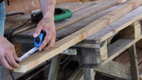 Un hombre marca el tamaño de una cinta métrica de metal en una barra de madera . — Vídeo de stock