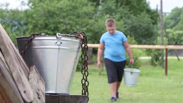 Defokussierter Junge mit einem Eimer in der Hand nähert sich einem Brunnen mit Wasser. — Stockvideo
