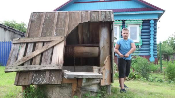 Pojken vrider handtaget på en brunn med vatten, sänker en hink i den. — Stockvideo