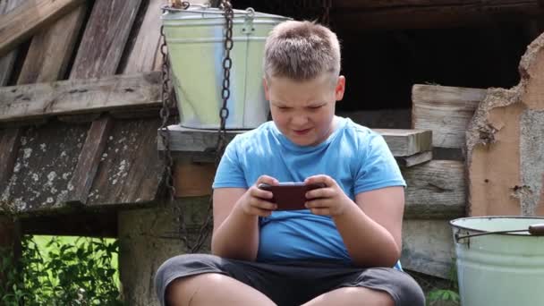 Nahaufnahme eines Jungen, der an einem Brunnen sitzt und emotional auf einem Smartphone spielt. — Stockvideo