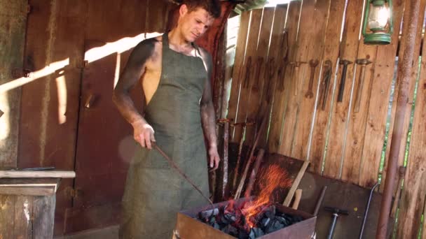 Mladý kovář míchá uhlíky pohrabáčem v kovárně.. — Stock video