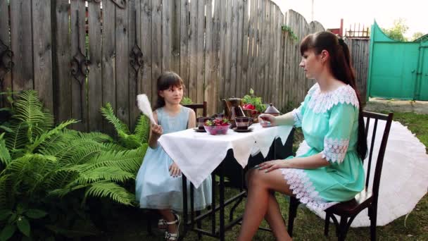 Malá holčička sedí u stolu se svou matkou na dvoře. — Stock video