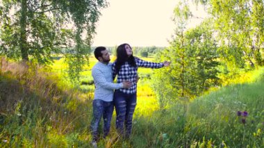 Kız yeşil çimlerin üzerinde genç bir adamın kollarında duruyor..