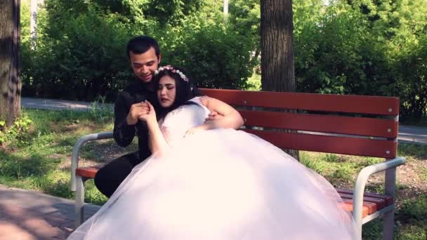 A vőlegény a padon ül, a menyasszony az ölében fekszik.. — Stock videók
