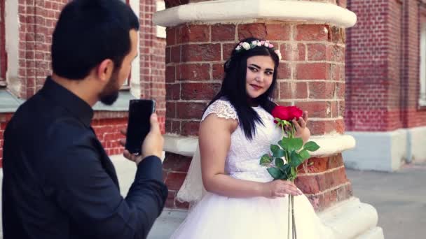 Чоловік фотографує дівчину з трояндами на телефоні . — стокове відео