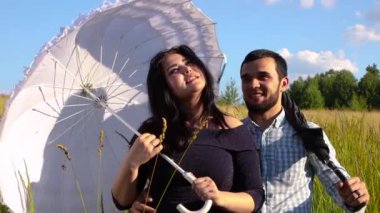 Genç bir adamın kollarında beyaz şemsiyeli bir kız gökyüzüne bakıyor..