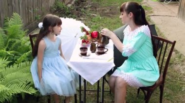 Anne ve kızı turkuaz elbiseler içinde masaya otururlar..