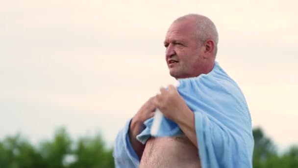 De man staat naakt en gooit een blauwe handdoek over — Stockvideo