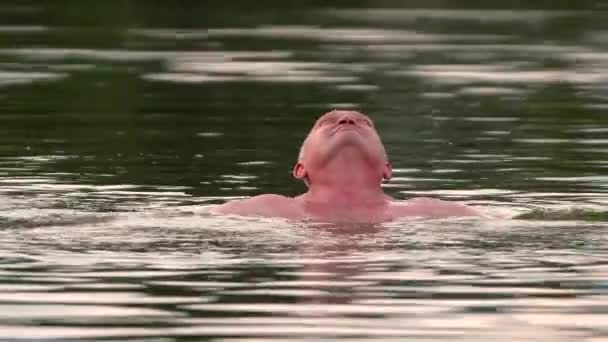男は髪の毛のない頭を水から出して泳いで. — ストック動画
