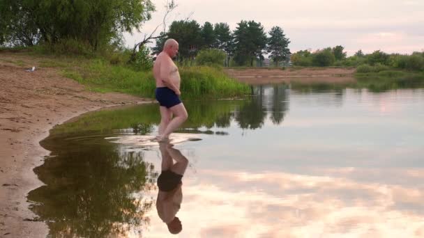 Um homem em alguns troncos de natação entra no lago para nadar. — Vídeo de Stock