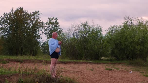 Un homme en maillot de bain se tient debout sur le rivage sablonneux et boit un verre. — Video