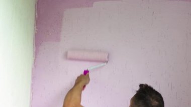 Duvarın tepesini pembeye boyayan bir adamın yakın çekimi..