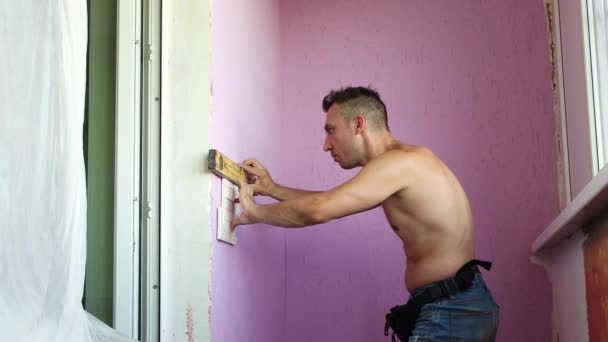 Een jongeman staat tegen de muur en brengt een liniaal aan op het oppervlak. — Stockvideo