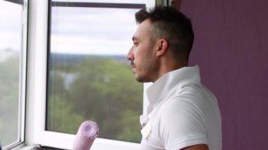 Beyaz tişörtlü genç bir adam plastik bir pencere açıyor..