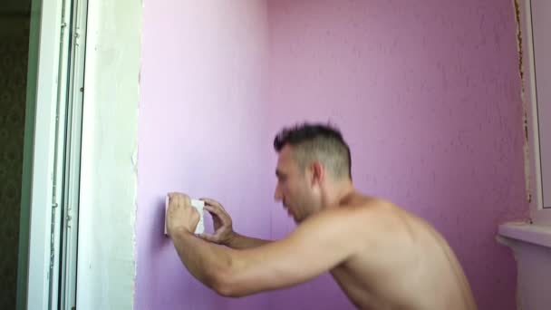 De man legt een tegel tegen de muur, hurkt en kijkt ernaar.. — Stockvideo