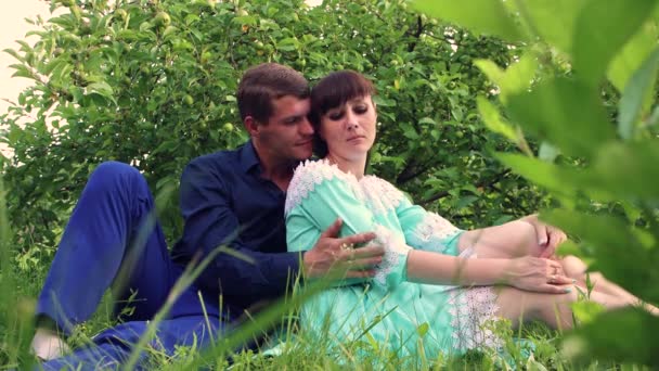Сидя в зеленом саду, мужчина ласкает девушку на плече. — стоковое видео