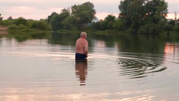 Молодий чоловік входить у прохолодну воду на резервуарі . — стокове відео