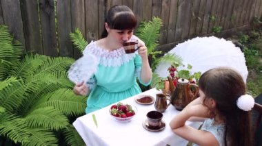 Bir kadın ve bir kız meyve ve çayla bir masada oturuyorlar.. 