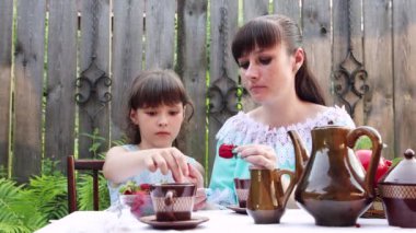 Anne ve kızı masada otururken çilek yiyorlar..