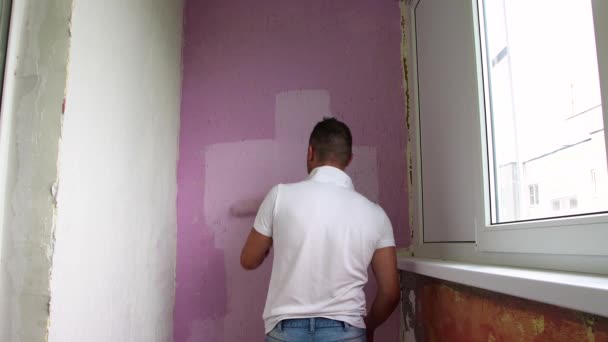 Sırtı beyaz tişörtlü genç bir adam duvarı boyuyor.. — Stok video