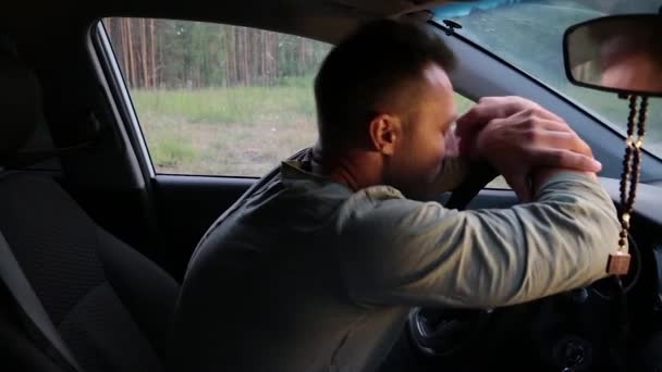Młody mężczyzna siedzi w samochodzie, trzymając kierownicę rękami.. — Wideo stockowe