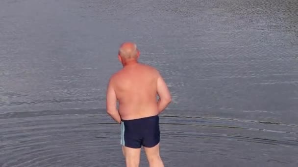 En man i några badbyxor går in i sjön lugnt och stilla — Stockvideo