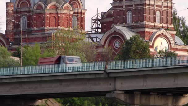 Un camión volquete cruza un puente de carretera con una iglesia al fondo. — Vídeos de Stock