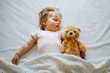 Küçük bebek yatakta uyuyan yumuşak oyuncak ayı sarılma, beyaz arka plan