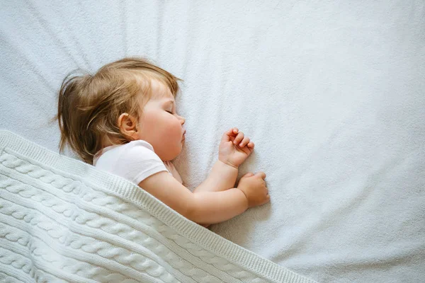 Sevimli küçük bebek evde battaniye ile kaplı yatakta huzur içinde uyuyor. Çocuk gündüz uyku programı