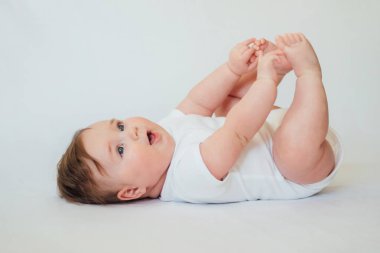 Beyaz arka planda beyaz giysiler giyen sırtüstü yatan küçük bebek 