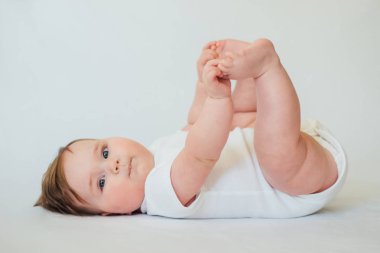 Beyaz arka planda beyaz giysiler giyen sırtüstü yatan küçük bebek 