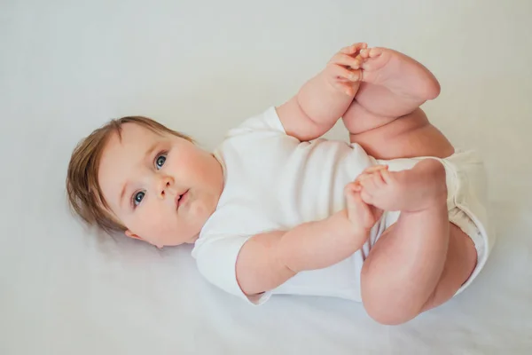 Little baby lying on back wearing white clothes on white background