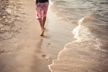 Bir adam gün batımında tatilde kum üzerinde yürüyor