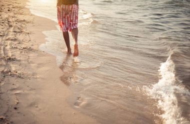 Bir adam gün batımında tatilde kum üzerinde yürüyor